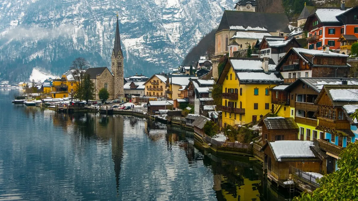 Hallstatt’ta çatıları karla kaplı renkli evler, sivri kuleli kilise ve karlı dağların yansıdığı göl