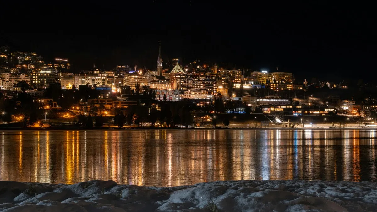 Gece ışıklarıyla aydınlanan St. Moritz kasabasının St. Moritz Gölü üzerindeki yansıması, ön planda kar