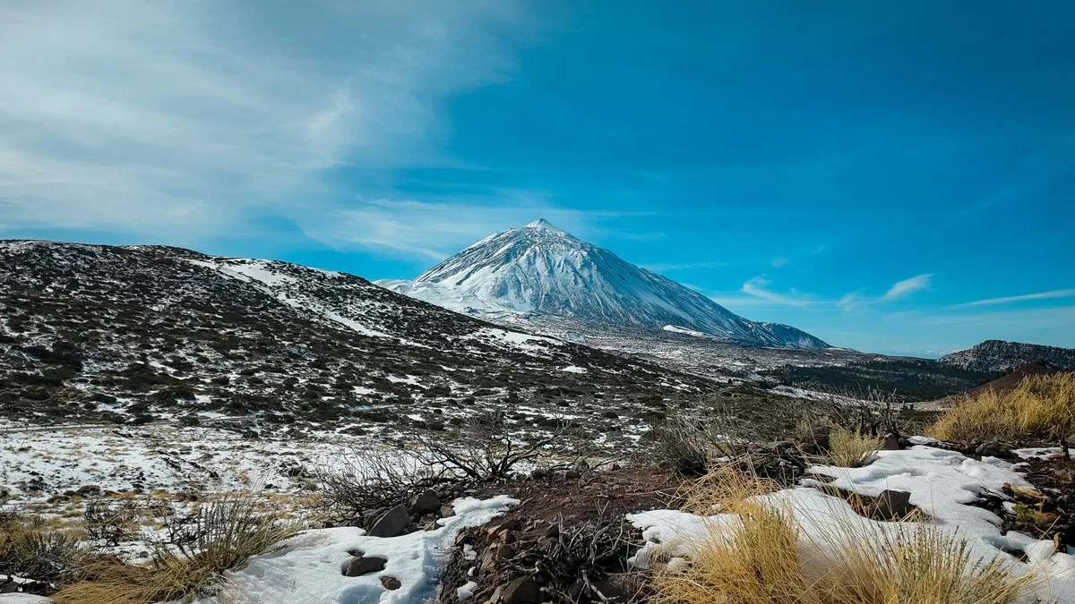 Tenerife’de mavi gökyüzü altında zirvesi karla kaplı Teide Dağı ve ön planda karla serpiştirilmiş volkanik arazi