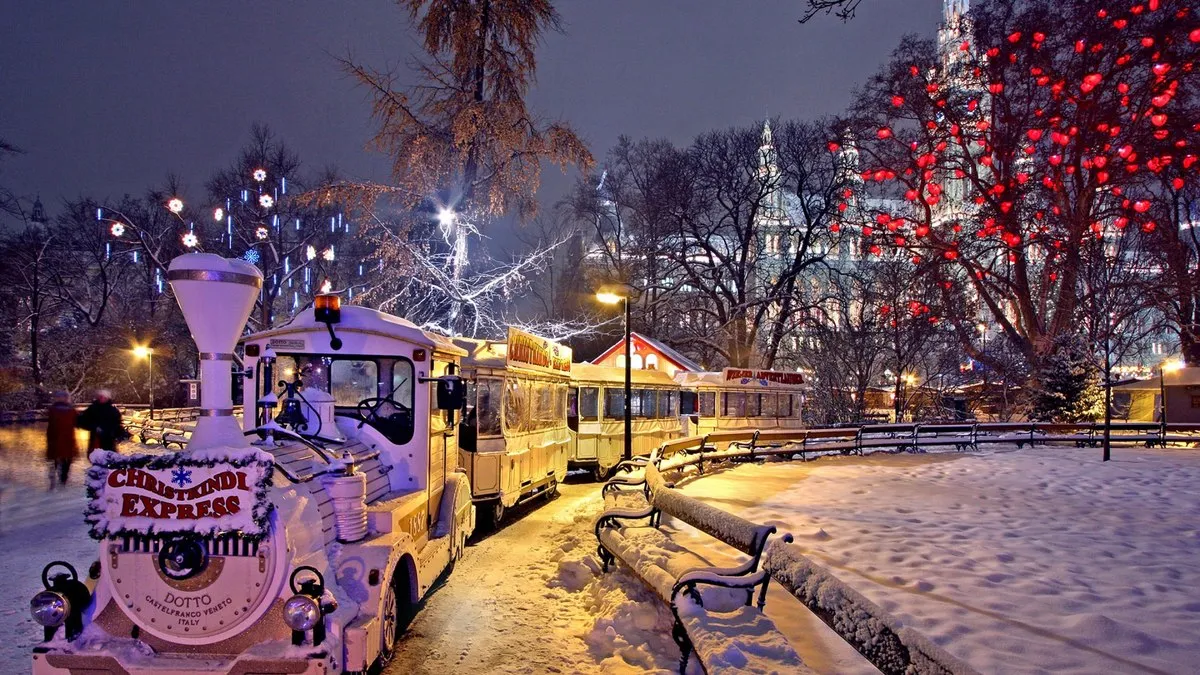 Viyana Belediye Binası önündeki Noel pazarında karla kaplı parkta Christkindl Express treni ve kalp şeklindeki ışıklarla süslü ağaç